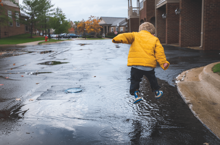 Toddler in yellow jacket jumping in puddle on deserted street. Learning A Language - New Baby New Paltz